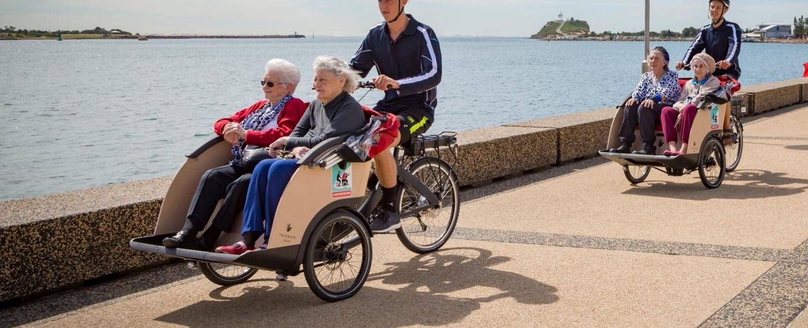 two cyclists with elderly passengers cycling along a path near water